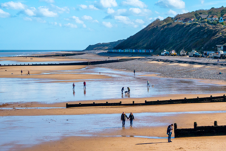 People spending the day on a beach on the Norfolk Coast, showing the sea and a hill in the background. style=